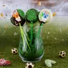 Soccer-themed cake pops arranged in a glass vase filled with artificial grass, with small soccer balls and cleats scattered on a grassy surface. Anteprima dell’immagine prodotto