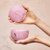 Hands holding a pink hair mask container and its lid. Voir les images du produit
