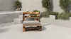 A wooden pallet chair with a gray cushion is placed on a patio next to a pool and some greenery. Produktbild-Vorschau