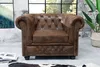 A brown Chesterfield armchair is placed in a room with a large window, a plant, and some books. Náhled obrázku produktu