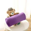 A teddy bear wearing a hat holds a rolled-up purple blanket on a white table. Produktbild-Vorschau