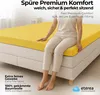 A person sitting on a bed with a yellow fitted sheet. Produktbild-Vorschau