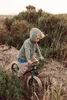 A young boy riding a balance bike through a grassy, outdoor area. Produktbild-Vorschau