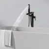 A black freestanding bathtub faucet with a handheld showerhead is shown filling a white bathtub. A white towel is draped over the side of the tub. Podgląd zdjęcia produktu