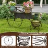 A metal bicycle-shaped plant stand with three baskets holding potted plants, set on a grassy lawn. Anteprima dell’immagine prodotto