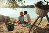A couple having a picnic by the river with a bicycle and a firewood holder. Produktbild-Vorschau