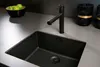 A black kitchen sink with a black faucet and a bowl of green apples on a gray countertop. Produktbild-Vorschau
