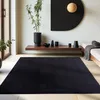 A modern living room with a black rug, wooden shelf with decor, and a large black semi-circle art piece on the wall.