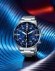 A close-up studio shot of a men's wristwatch with a blue dial, set against a textured, wavy background with blue and red lighting. Produktbild-Vorschau