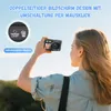 A woman is holding a digital camera and taking a selfie outdoors. Anteprima dell’immagine prodotto