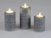 Three LED candles with a gray, textured surface and white wavy lines, lit with a warm glow, are arranged on a light gray background. Produktbild-Vorschau