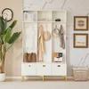 A white entryway cabinet with drawers and shelves, decorated with gold accents and various items like books, a camera, hats, and clothing. Anteprima dell’immagine prodotto