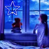 A young girl in pajamas looks out a window at a starry night sky, with a teddy bear sitting on books on the windowsill. Produktbild-Vorschau
