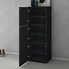 A black shoe cabinet with its doors open, revealing six shelves. The cabinet is placed against a gray textured wall, with a pair of beige shoes visible on the floor in front of it. Produktbild-Vorschau