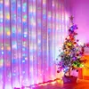 A decorated Christmas tree stands next to a curtain illuminated with colorful lights. Produktbild-Vorschau