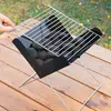 A hand is shown placing a grill grate on a portable charcoal grill filled with briquettes, set on a wooden table outdoors. Náhled obrázku produktu