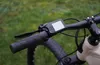 A close-up view of an electric bicycle's handlebars and display screen, set against a blurred green grassy background. Produktbild-Vorschau