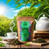 A bag of tea, a cup of tea, and a teapot are arranged on a wooden table with a natural outdoor background. Náhled obrázku produktu