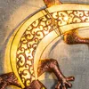 A close-up of a decorative gecko-shaped wall light with intricate scrollwork illuminated from behind. Produktbild-Vorschau
