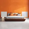 A modern bedroom with an orange wall, a bed with orange and white pillows, and two white panels on the wall. Anteprima dell’immagine prodotto