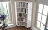 A white corner bookshelf filled with books and a plant, placed next to a window with a view of trees. Produktbild-Vorschau