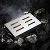A stainless steel smoker box filled with wood chips, placed on a bed of hot charcoal, with smoke rising from it. Produktbild-Vorschau