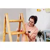 A woman wearing headphones is working on a wooden ladder, holding a tool. Produktbild-Vorschau