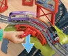 A child's hand is operating a toy train track mechanism, with two toy trains on the tracks. One train is purple and white, and the other is blue and red. Náhľad obrázku produktu