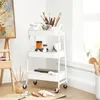 An artist's studio with a white rolling cart filled with art supplies, next to an easel with a painting. Náhled obrázku produktu
