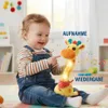 Lächelndes Baby in Jeans-Latzhose berührt ein gelbes leuchtendes Giraffenspielzeug mit Musiknoten, die darum schweben Podgląd zdjęcia produktu