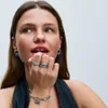 A woman wearing jewelry, including rings and earrings, and a denim top. Produktbild-Vorschau