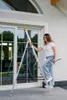 A woman is using a ladder to clean a large window. Anteprima dell’immagine prodotto
