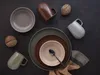 A top-down view of a set of ceramic dishes and mugs arranged on a dark surface. Produktbild-Vorschau