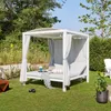 A white outdoor daybed with gray curtains and cushions is set up on a green lawn, surrounded by trees and bushes. Produktbild-Vorschau
