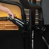 A hand is placing a black water bottle into a holder on a black exercise machine. Produktbild-Vorschau