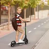A young boy is riding a scooter on a paved path next to a fence and trees. Náhľad obrázku produktu