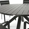 A close-up view of a round outdoor dining table with a slatted top and a dark, angular base. Chairs are partially visible in the background and foreground. Produktbild-Vorschau