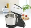 A white and black electric hand mixer with a stainless steel bowl is shown in a kitchen setting, with cakes in the background. Produktbild-Vorschau