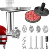A collection of kitchen appliance attachments and accessories, including a meat grinder attachment, various grinding plates, sausage stuffing tubes, a cleaning brush, and a burger press with ground meat. Produktbild-Vorschau