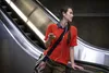 A young woman stands on an escalator, holding a smartphone and wearing earbuds. Anteprima dell’immagine prodotto