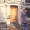 A person walks past a mailbox mounted on the side of a building. Náhled obrázku produktu