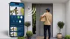 A delivery person is at a front door, and a smartphone displays a live feed from a security camera. Anteprima dell’immagine prodotto