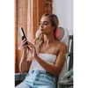A woman is sitting in a chair, holding a remote control and using a neck massager. Produktbild-Vorschau