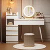 A white vanity table with gold accents and a lighted mirror, set up in a room with decorative wall paneling and a stool. Produktbild-Vorschau