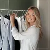 A woman is holding up clothes on hangers in a closet. Produktbild-Vorschau