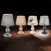 Four table lamps are displayed in a row against a dark, gradient background. Produktbild-Vorschau