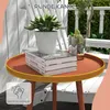 A round garden side table with books, a potted plant, and a drink on it, placed outdoors on a wooden deck with white chairs in the background. Produktbild-Vorschau