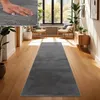 A long, dark gray rug is laid out on a polished wooden floor in a hallway. Sunlight streams in from large windows, illuminating two chairs and a wooden cabinet. Voir les images du produit