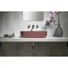 A modern bathroom vanity with a maroon red oval basin sink, wall-mounted faucets, and a vase with flowers. Produktbild-Vorschau