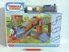 The image shows the packaging of a Thomas & Friends toy train set, featuring Thomas the Tank Engine and his carriages on a track with a bridge and a loading crane. Náhled obrázku produktu